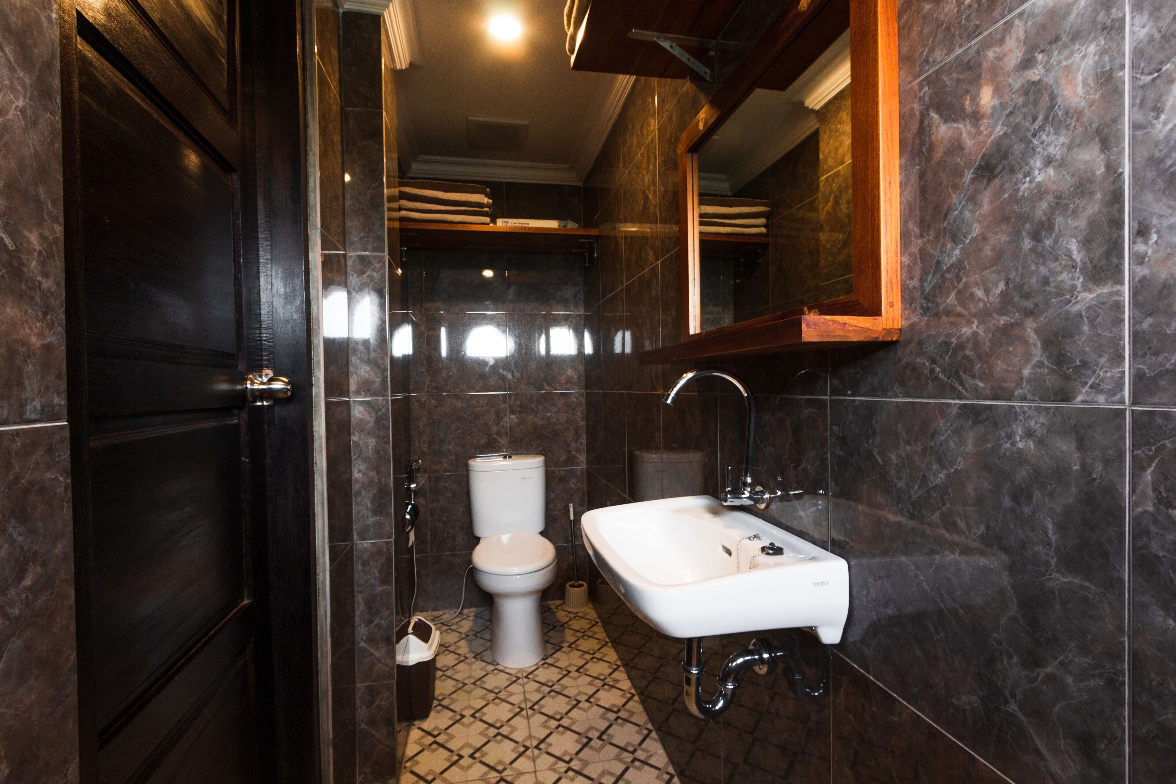 Ein modernes Badezimmer mit einer dunkelholznen Tür, einer weißen Toilette, einem weißen Waschbecken und einem Spiegel über dem Waschbecken.