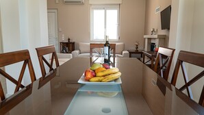 Un coin repas avec une table en verre, des chaises en bois et un plateau de fruits.