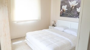Une chambre à coucher avec un grand lit, une table de chevet, une lampe et un tableau représentant des fleurs accroché au mur.