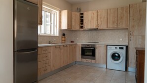 Une cuisine avec des meubles en bois, un réfrigérateur en acier inoxydable, un four encastré et un lave-linge à chargement frontal.