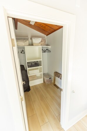 Un dressing accessible sans porte, avec un plafond en bois, des étagères blanches et un petit tableau encadré accroché au mur.