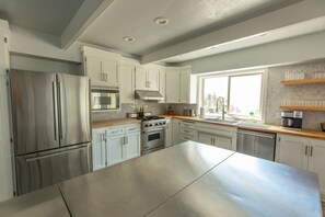 A modern kitchen with stainless steel appliances, white cabinetry, and a large island. - Mervue Estate - Luxury ocean view on 60 acres (Gold Beach)