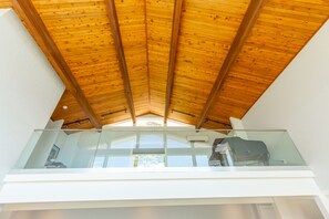 Un interior moderno con techo de madera, balcón de cristal y vistas al exterior.