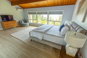 Un dormitori amb un llit gran, televisió, sofà i finestra amb vista a arbres.