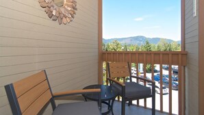 A balcony with a wooden bench and a small round table, overlooking a parking area and mountains. - Heart of the Village. Newly renovated , modern décor throughout, Central AC just installed 2024 (Whistler)
