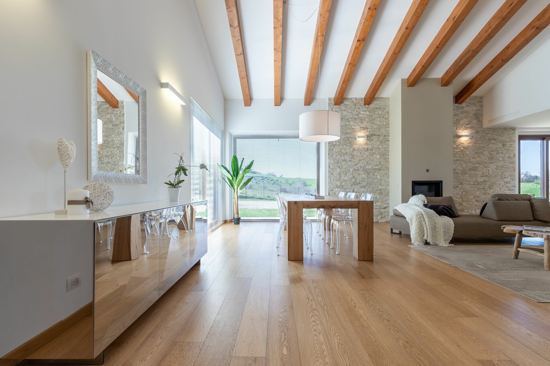 A spacious living area with a wooden dining table, clear chairs, a sofa, and a fireplace.