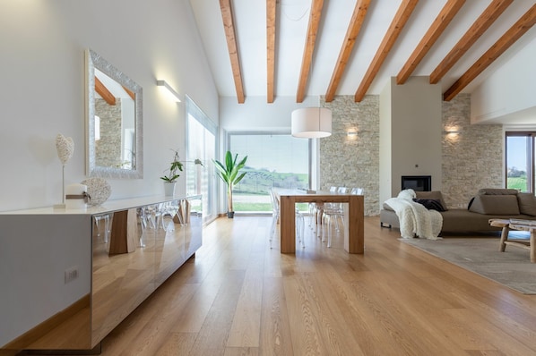 A spacious living area with a wooden dining table, clear chairs, a sofa, and a fireplace.