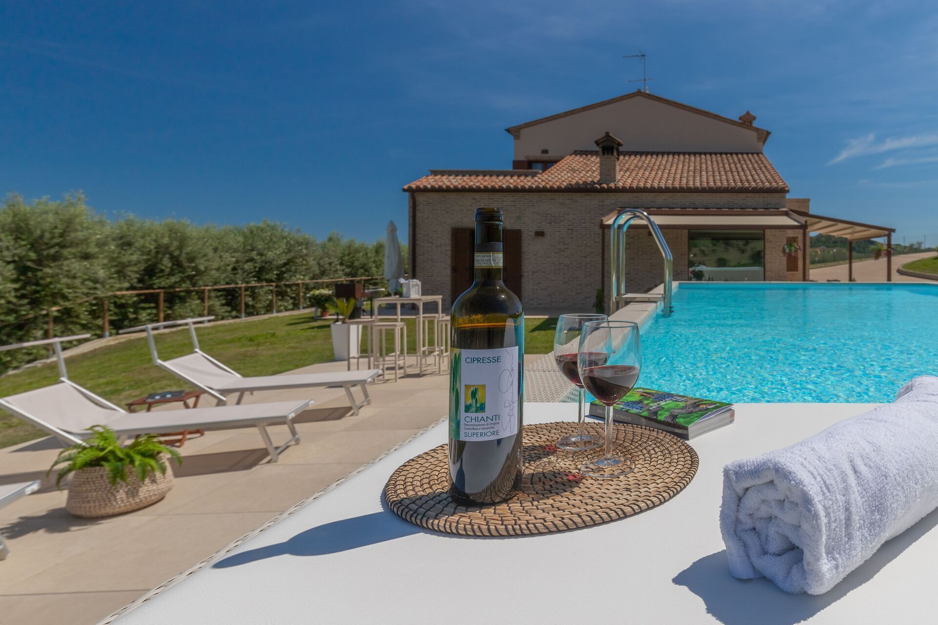 A poolside setting with a bottle of wine, glasses, and a towel.