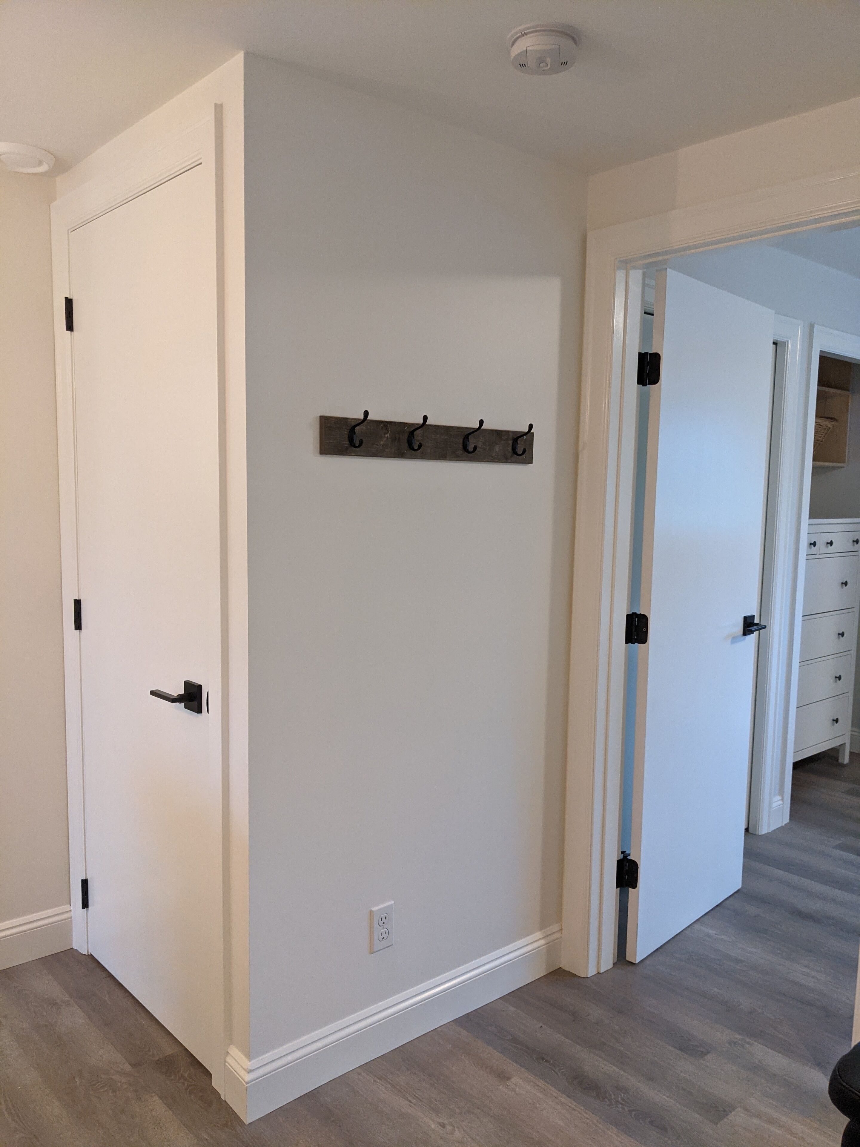 A hallway with a white door, a coat rack, and a partially open door leading to a kitchen area.