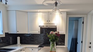 Eine moderne Küche mit weißen Schränken, einer zentralen Kochinsel, einer Blumenvase und einer Hängeleuchte.