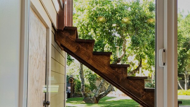 Eine Holztreppe führt nach draußen zu einem Rasen mit Bäumen.