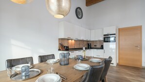 A dining area with a wooden table set for four, surrounded by leather chairs. A kitchen with white cabinets and wooden accents is visible in the background. - Stylish penthouse with shared sauna and lift (Walchen)