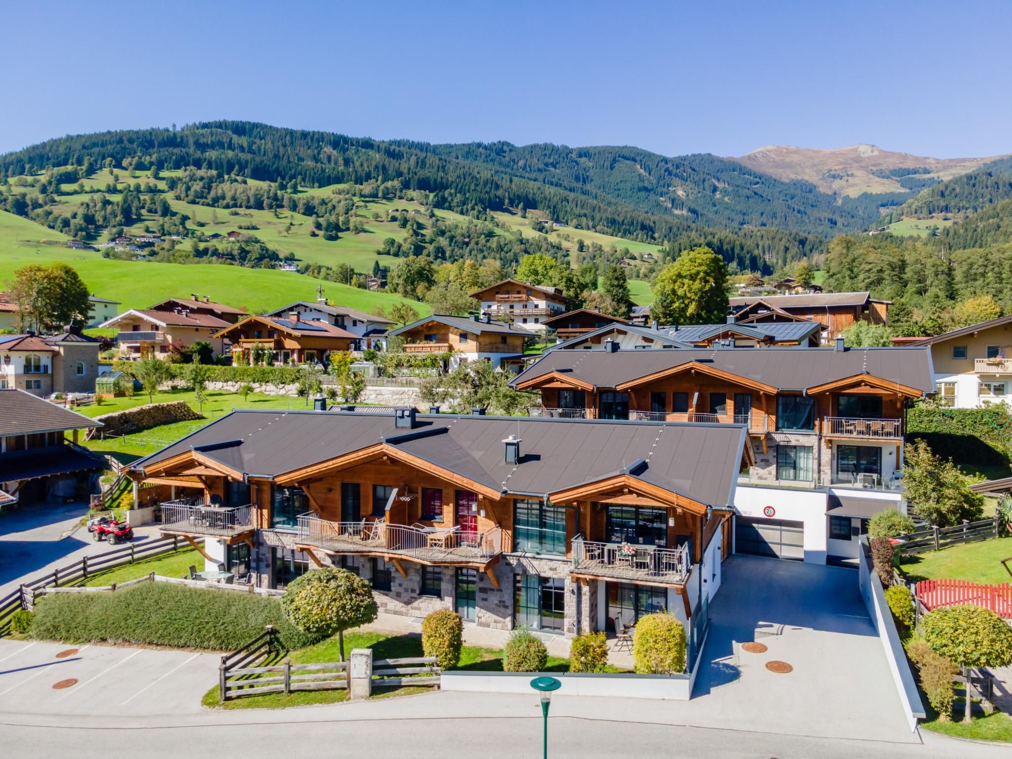 En grupp av träbyggnader i chaletstil med balkonger, belägna mot en bakgrund av grönskande kullar och berg.