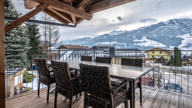 A wooden deck with a table and chairs, overlooking a snowy mountain landscape. - Stylish penthouse with shared sauna and lift (Walchen)