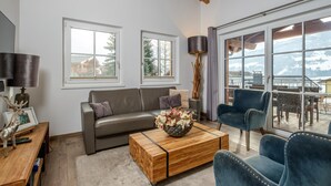 A modern living room with a sofa, a coffee table, and a chair. There are two windows and a view of a snowy mountain. - Stylish penthouse with shared sauna and lift (Walchen)