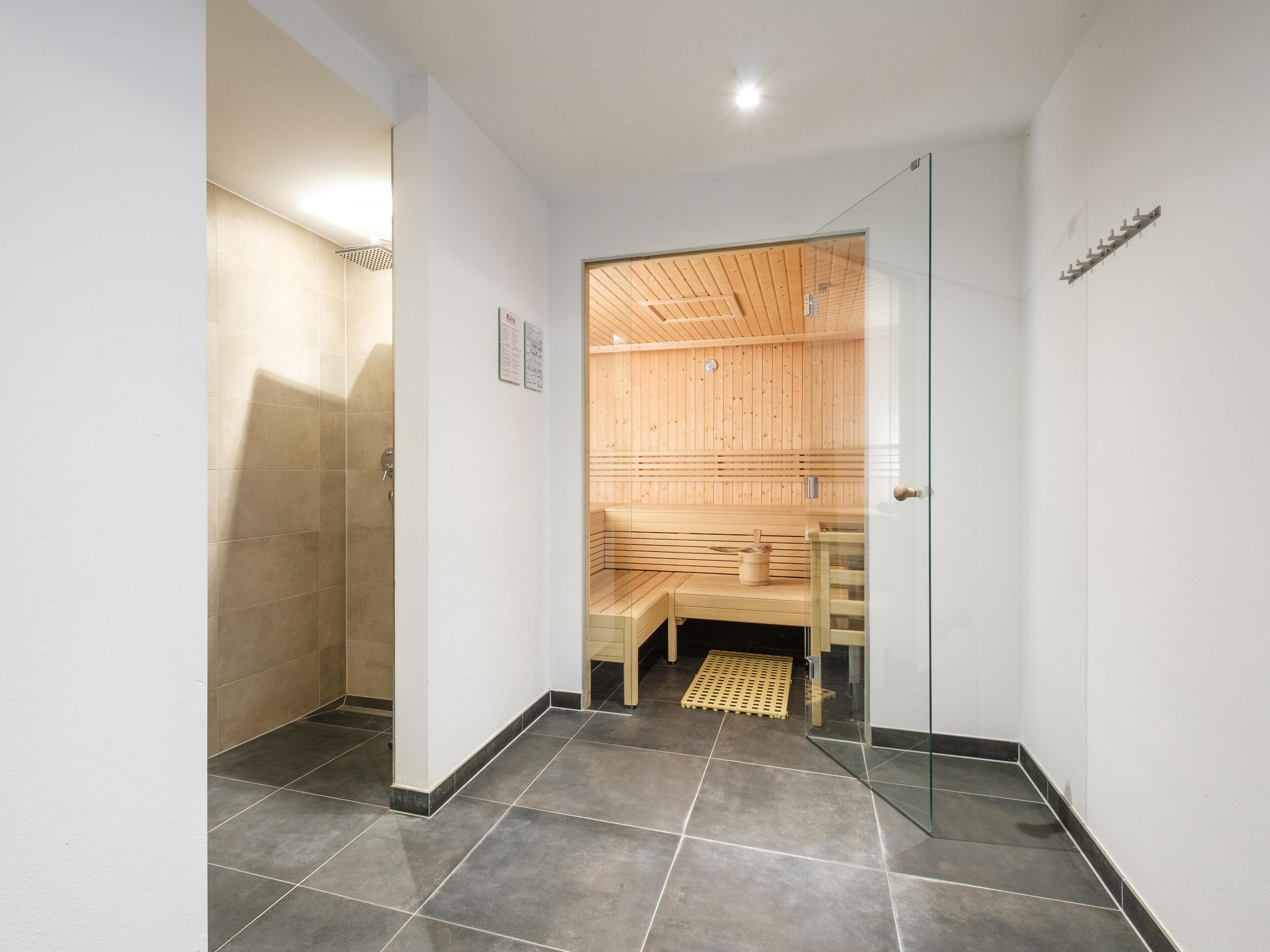 A modern bathroom with a shower, a glass door leading to a sauna area with wooden benches.