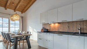 A modern kitchen with white cabinets, a wooden ceiling, and a dining area with a table and chairs. - Stylish penthouse with shared sauna and lift (Walchen)
