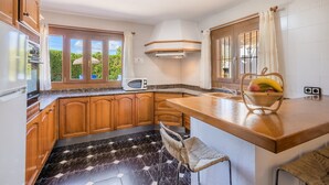A kitchen with wooden cabinets, a microwave, a sink, and a fruit basket on the counter. - Vacation Villa 'Can Serra' with Private Pool, Mountain Views, Terrace & Garden (Puerto Pollensa)