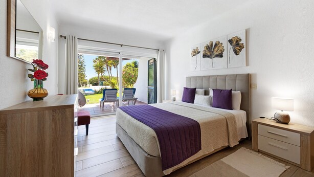 Quarto com cama, mesa de cabeceira e vista para o exterior.