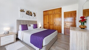 Quarto com cama, mesa de cabeceira, penteadeira, guarda-roupa de madeira e espelho.