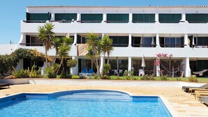 Vista da piscina de um hotel, com uma piscina grande, várias varandas e áreas de estar ao ar livre.