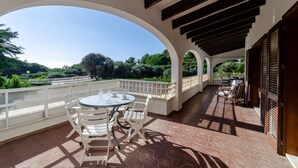 A covered outdoor area with a table and chairs, a view of greenery, and a railing. - Wonderful Villa “Villa Las Palmeras” with Sea View, Pool, Wi-Fi, A/C, Garden & Terrace (Binibequer)