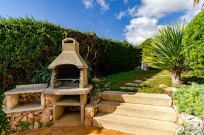Un barbecue en pierre, accessible par des marches, entouré de verdure et surplombant un ciel dégagé.