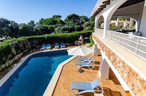 Une piscine entourée de murs en pierre et de verdure, avec des chaises longues et des parasols.