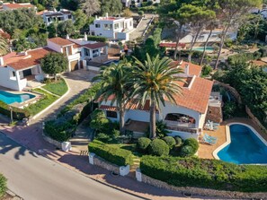 Un quartier résidentiel comprenant plusieurs maisons, une maison principale dotée d’une piscine et des jardins bien entretenus.