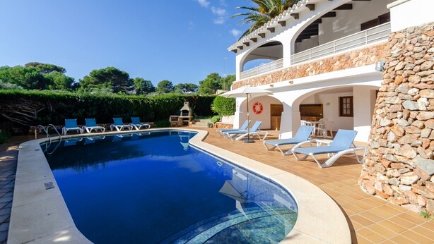 A swimming pool with lounge chairs, a stone wall, and a building with a balcony. - Wonderful Villa “Villa Las Palmeras” with Sea View, Pool, Wi-Fi, A/C, Garden & Terrace (Binibequer)