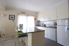 Una cocina con gabinetes blancos, lavavajillas integrado, microondas y refrigerador.