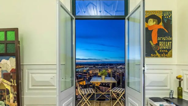 Une chambre avec un balcon donnant sur une vue panoramique de la ville au crépuscule.
