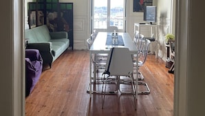 Un coin repas avec une table et des chaises, un canapé vert et une vue dégagée sur l’extérieur grâce à une grande fenêtre.