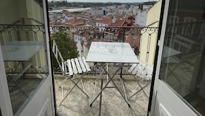 Un balcon avec une table et des chaises, donnant sur un paysage urbain avec des immeubles et une rivière.