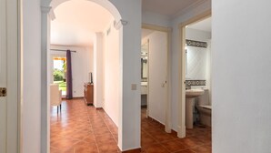 Un couloir doté d’un sol carrelé, une porte donnant sur une salle de bain et une vue sur un jardin par une porte ouverte.