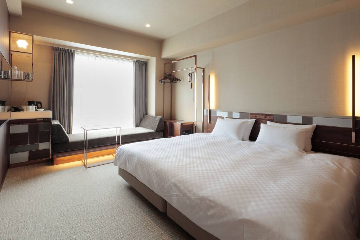 Una habitación de hotel moderna con una cama grande, mesitas de noche, un escritorio con silla, una ventana con cortinas y un armario empotrado.