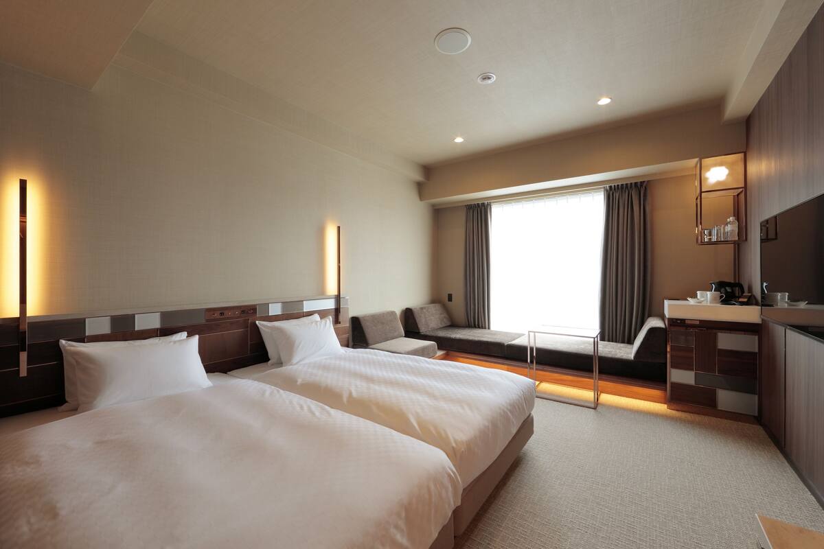 Habitación de hotel con dos camas grandes, una zona de estar, una mesita y una kitchenette.