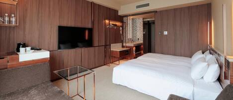 A modern hotel room with a large bed, a TV, a desk, and a seating area.