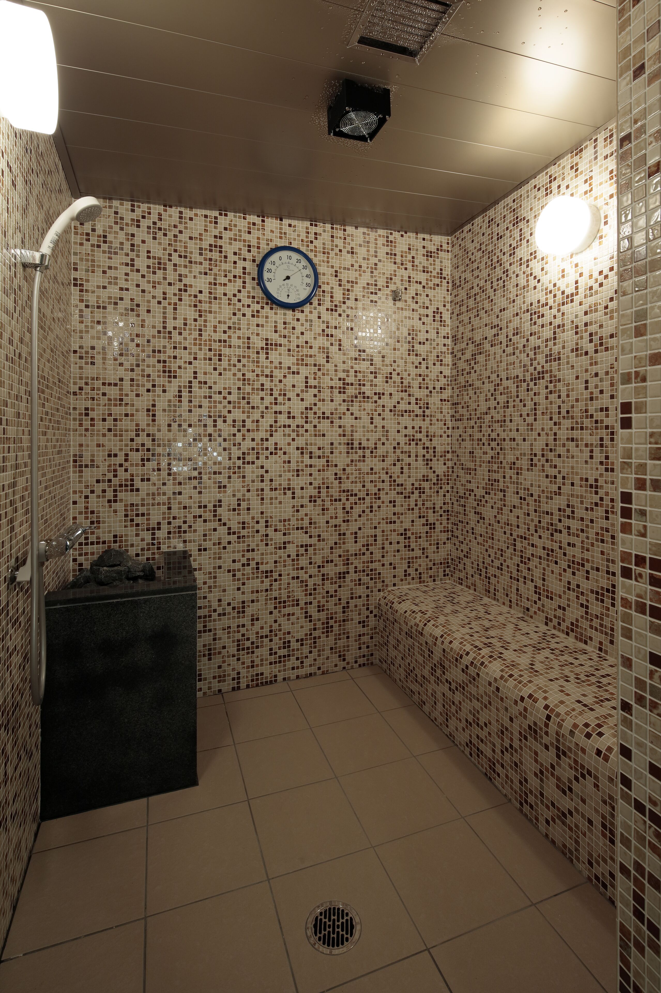 A small, tiled shower room with a clock on the wall, a bench, and a small sink.