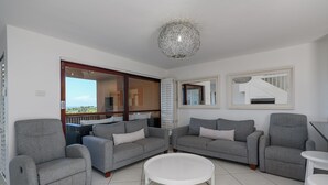 Un salon avec des canapés gris, une table basse blanche et une vue sur l’extérieur.