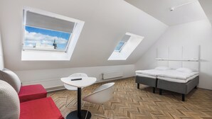 A modern, compact room with a sloped ceiling, two skylights, a bed, a small table with a chair, and a radiator. - Omena Hotel Turku Kauppiaskatu (Turku)