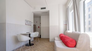A modern hotel room with a white sofa, a red pillow, a white chair, and a small table. - Omena Hotel Turku Kauppiaskatu (Turku)