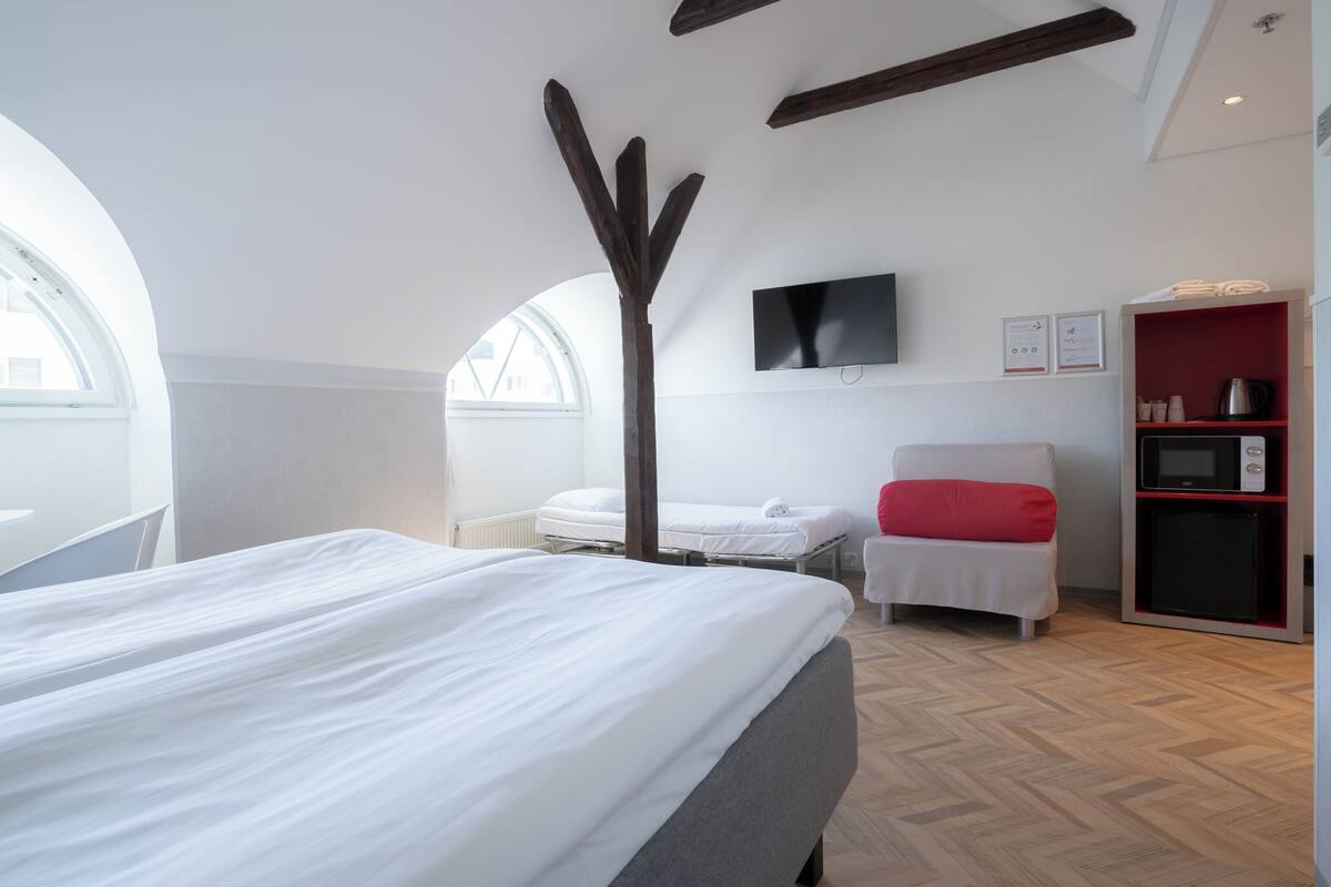 A modern hotel room with a large bed, a small desk, a TV, and a kitchenette.