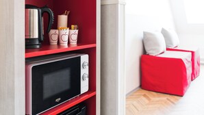 A red-framed shelf with a kettle, stacked cups, and a microwave. - Omena Hotel Turku Kauppiaskatu (Turku)