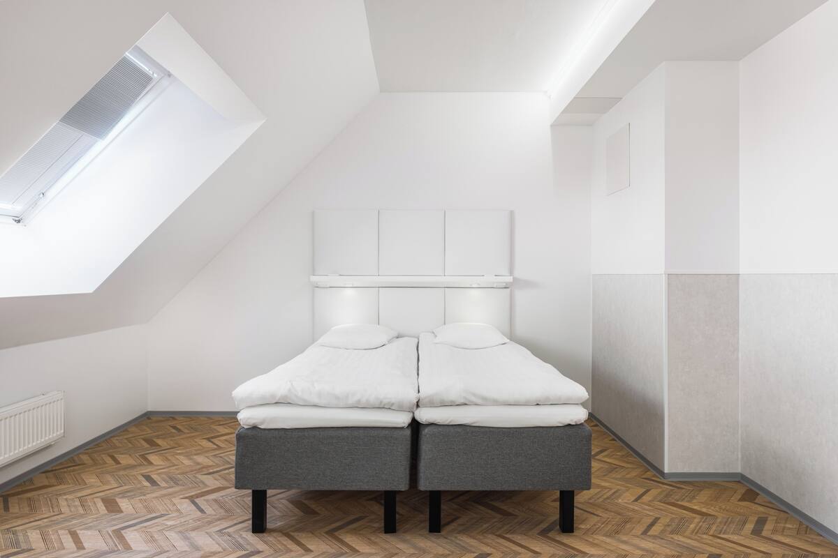 A modern, minimalist room with a sloped ceiling, a built-in bench at the foot of a bed, and a skylight above.
