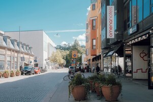 Vista de la calle con un hotel llamado 'omenahotels' a la derecha, que presenta una fachada moderna con grandes ventanales y un letrero.