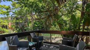 Une terrasse en bois, dotée de meubles en osier et d’une rambarde en verre, qui offre une vue sur un jardin.
