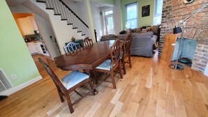 Un coin repas avec une table et des chaises en bois, une cuisine à l’arrière-plan et un mur en briques.