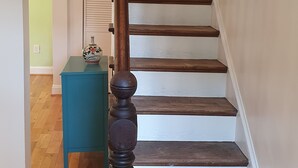 Un escalier en bois, avec des murs blancs et une petite table d’appoint de couleur turquoise.