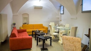 Ein Wohnzimmer mit hoher, gewölbter Decke, einem gelben Sofa, einem roten Sofa, einem Glastisch mit Stühlen und einem Kamin.